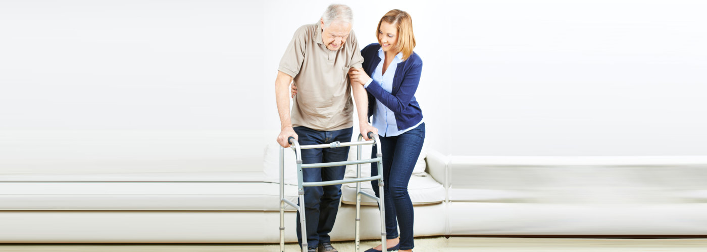 caregiver guiding a senior man to walk